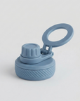 A dusty blue reusable bottle cap with a flip-up loop lid, shown on a light gray background.